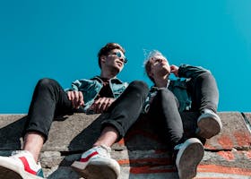 Two young people sitting on a stone wall under a vibrant blue sky, enjoying a sunny day together.