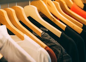 A close-up view of a row of clothes on wooden hangers, showcasing various fabrics and colors in a wardrobe setting.